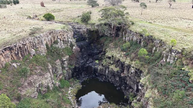Aerial drone shot flying over a creek flowing into the deep rocky gorge of lal lal falls, victoria