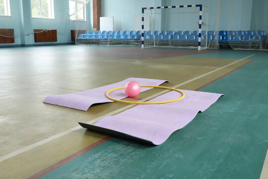 Fitness mat with hula hoop and pink ball on floor inside sports hall gym court. Indoor rhythmic gymnastics training, active healthy amateur athlete hobby lifestyle concept. Copy space wallpaper