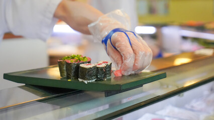 Sushi chef hand in glove placing fresh maki rolls on a plate at a restaurant counter © Creativa Images