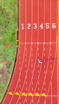 Aerial view of a red running track with white lane numbers and a lone runner at the Instituto Tecnologico de Merida, Yucatan, Mexico.