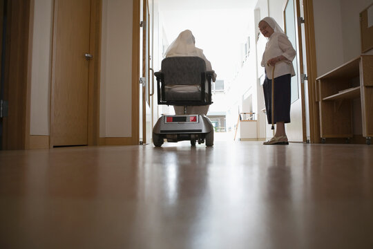 Rear view of a nun sitting in a motorized wheelchair with another nun standing beside her in a