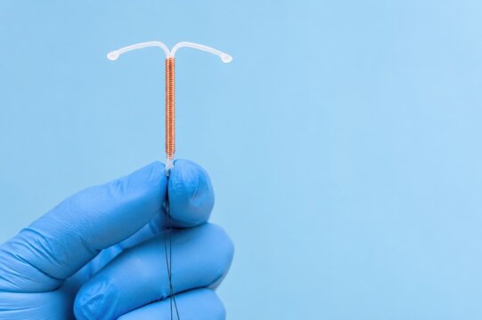 Intrauterine device held in gloved hand on blue background. Contraception method, reproductive health, family planning and women's healthcare concept