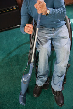 Man with spinal cord injury in a wheelchair rewinding power cord on vacuum cleaner
