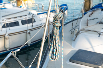 Horizontal nautical scene in a marina with several sailboats docked, focusing on a coiled rope hanging from a metal pole on a boat © Juli