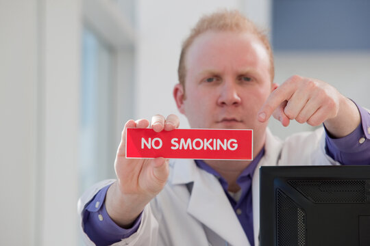 Doctor holding a red 'no smoking' sign and pointing to it with a serious face