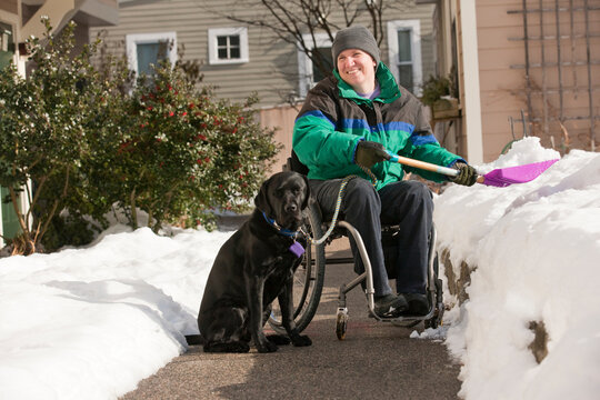 Woman with multiple sclerosis shoveling snow in a wheelchair with a service dog
