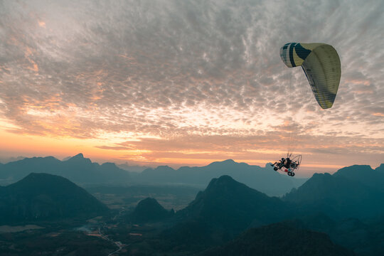 Powered Paraglider Flying Above Karst Mountains at Sunrise in Vang Vieng, Laos
