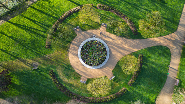 Aerial view of a circular flower bed surrounded by sandy paths, green lawns, and trees casting long shadows in a public park Morlaix, Brittany, France.
