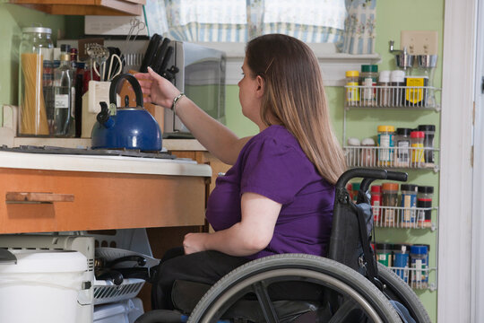 Woman with Spina Bifida in a wheelchair positioning a kettle in the accessible kitchen