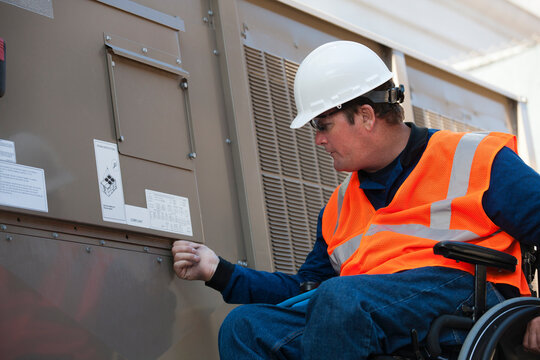 Facilities engineer in a wheelchair opening inspection plate of commercial air conditioning system