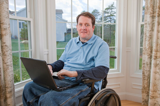 Businessman with spinal cord injury in a wheelchair working on a laptop with disabled hands