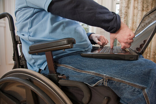Businessman with spinal cord injury in a wheelchair working on a laptop with disabled hands