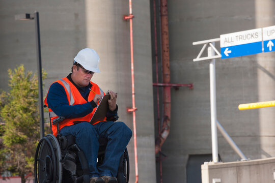 Facilities engineer in a wheelchair inspecting outdoor bulk storage tanks and recording data