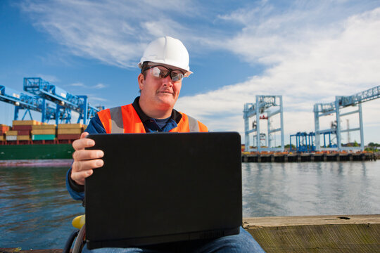 Transportation engineer in wheelchair recording data on laptop at shipping port