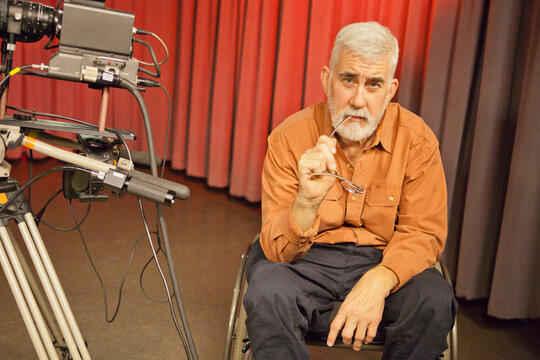 Man in wheelchair with muscular dystrophy beside a TV camera in studio