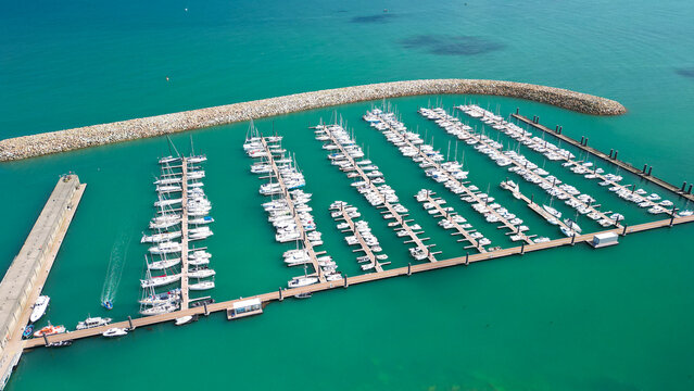 Aerial view of the Port de Roscoff marina featuring rows of white yachts and sailboats docked in turquoise waters protected by a stone breakwater in Roscoff, Bretagne, France.