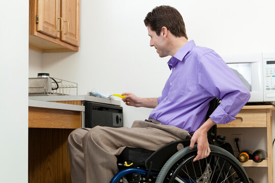 Man in wheelchair with spinal cord injury dusting in an accessible kitchen