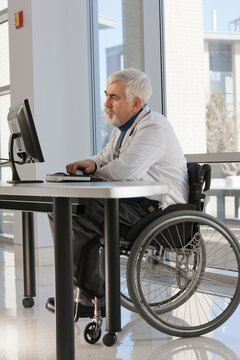 Doctor with muscular dystrophy in wheelchair studying information on his computer