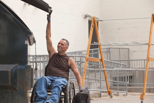 Loading dock worker with spinal cord injury in a wheelchair putting a bag in the dumpster