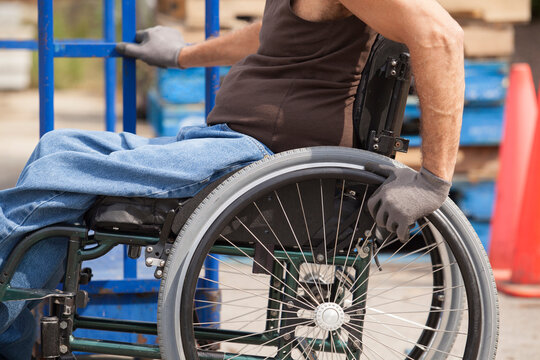 Loading dock worker with spinal cord injury in a wheelchair moving a hand truck