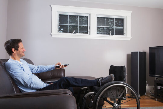 Man with spinal cord injury with leg in wheelchair watching TV with remote