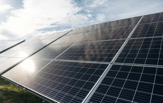 Solar panels installed in a green field under a bright sky, showcasing renewable energy technology with reflections on the glass surface and grass in the foreground