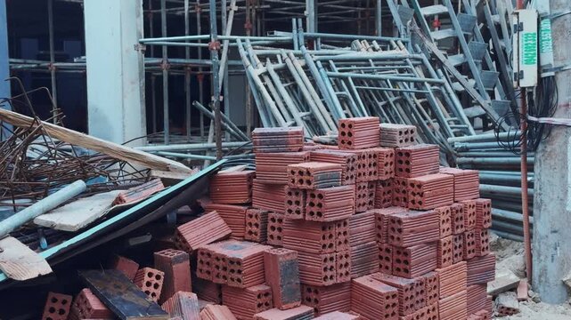 Construction site showing piles of red bricks, scaffolding, rebar, and building debris, representing the industrial process of urban development and growth