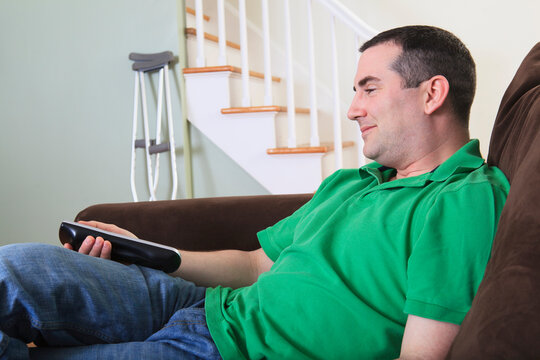 Man after anterior cruciate ligament (ACL) surgery using a TV remote at home