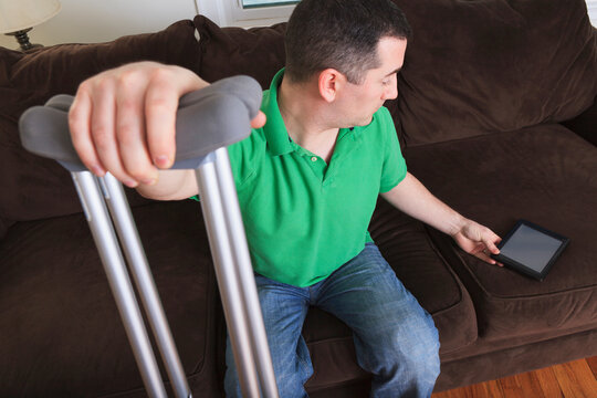 Man after anterior cruciate ligament (ACL) surgery with crutches and an digital tablet at home