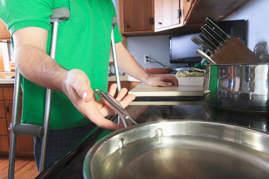 Man after anterior cruciate ligament (ACL) surgery with crutches cooking in the kitchen