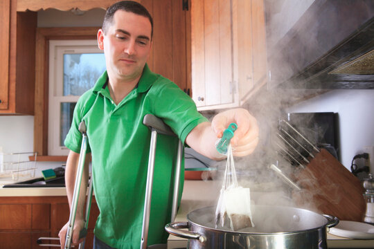 Man after anterior cruciate ligament (ACL) surgery with crutches making tea in the kitchen