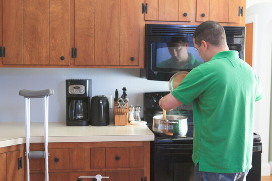 Man after anterior cruciate ligament (ACL) surgery with crutches cooking in the kitchen