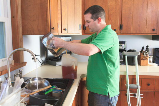 Man after anterior cruciate ligament (ACL) surgery with crutches making tea and doing dishes in the