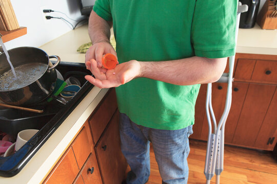 Man after anterior cruciate ligament (ACL) surgery with crutches taking medicine in the kitchen