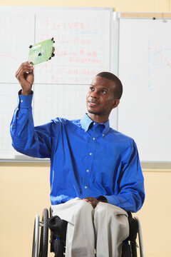 Engineering student sitting in a wheelchair from Spinal Meningitis, examining microprocessor