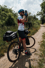 Naklejka premium Cyclist with a loaded gravel bicycle taking a photo on a countryside trail. Adventure travel and outdoor exploration concept