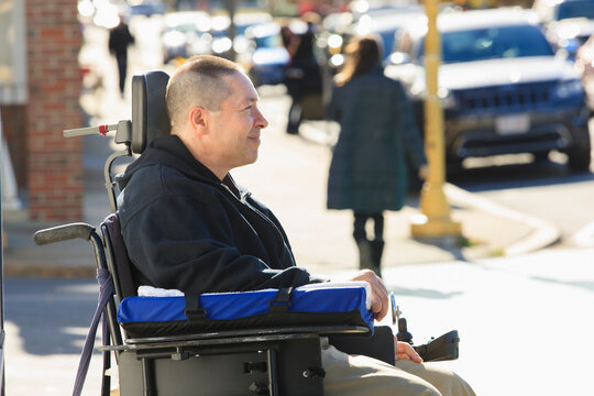 Man with spinal cord injury and arm with nerve damage in motorized wheelchair crossing public street