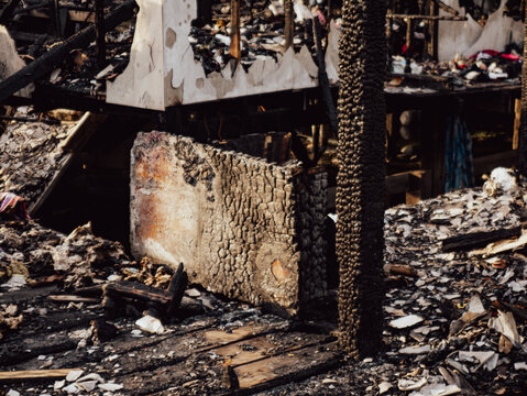 Fire disaster aftermath scene showing burned destroyed house interior with charred wood debris ash and collapsed furniture in residential fire