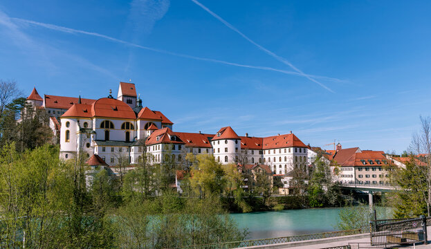 Beautiful view of St Mang Abbey and Hohes Schloss castle over the turquoise Lech river in Fussen, historic architecture and scenic town landscape under a blue sky, Bavaria, Germany.