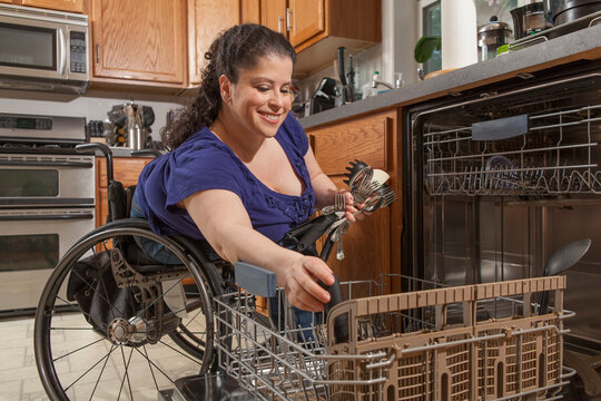 Woman with Spina Bifida using the dishwasher in kitchen