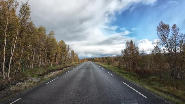 Camper van traveling on an empty road through the autumn landscape of northern Norway