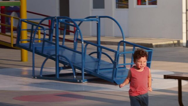 Caucasian toddler boy running at clean outdoor playground, park with see-saw, slide, slope etc. - released fit for commercials
