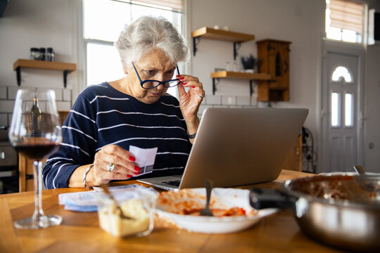 Senior woman reviewing finances on laptop in home kitchen
