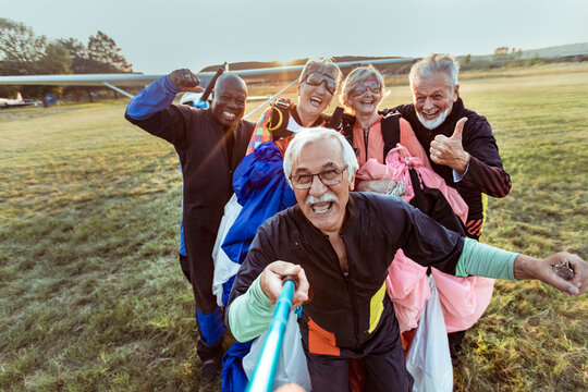Happy senior friends taking skydiving selfie at airfield after landing
