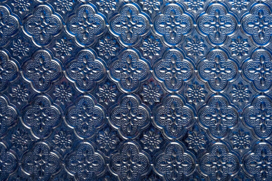 Elegant cobalt blue textured glass with a repeating vintage floral geometric pattern. Glossy embossed surface creates a sophisticated tactile background with deep sapphire and indigo tones.