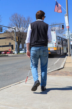 Young blind man with cane heading toward a bus stop