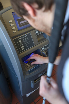 Young blind man with cane using a bank ATM