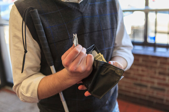 Young blind man with cane counting his money