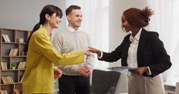 Agent and couple celebrate apartment viewing handshake. They confirm agreement, review contract steps, and plan next actions in a bright home setting. Clear concept of trust and closing.