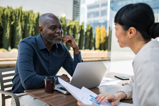 Two business professionals meeting at outdoor cafe with laptop